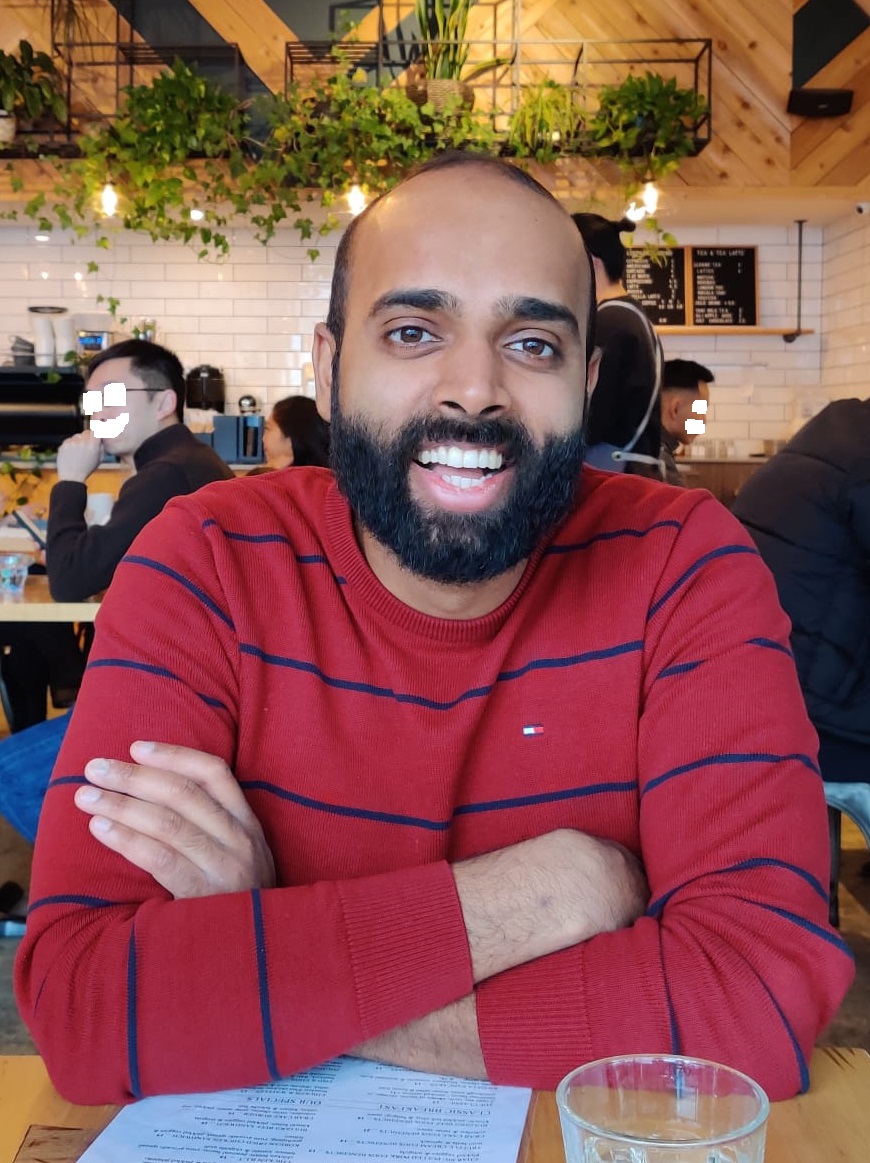 Janarth seated at a single wooden table inside Elephant Grind Coffee before eating delicious brunch!
                                In the background you can see the decor of the Elephant Grind Coffee restaurant.